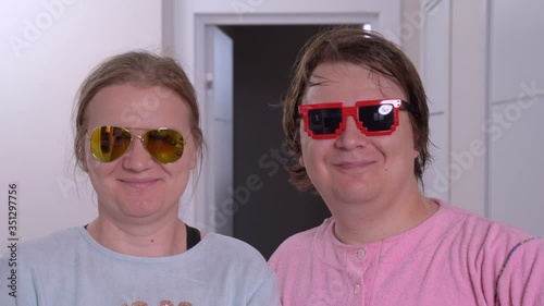 Young pair, man and woman in casual with face expression of utter amazement or shock, open mouths, looking at something. After the both put on funny colorful glasses, knowingly smiling and nodding photo