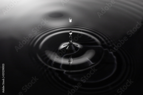 Close-up of a water drop impact on black background with water surface, causing rings on the surface.