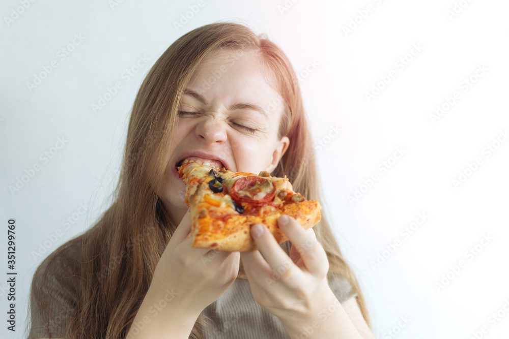 Young caucasian woman girl hungrily biting eating a slice of pizza with a funny face