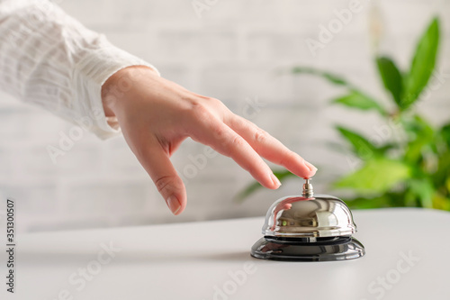 Hand of guest ringing in silver bell. reception desk with copy space. Hotel service. Selective focus