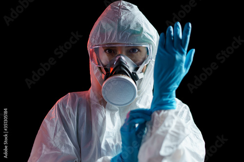 Person in protective suit wearing rubber gloves on dark background.