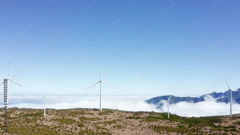 4K drone video of wind generators revolving on hill with mountains and blue sky in background. Environment conservation concept. Alternative means of energy concept footage. 4K drone video of wind generators revolving on hill with mountains and blue sky in background. Environment conservation concept. Alternative means of energy concept footage.