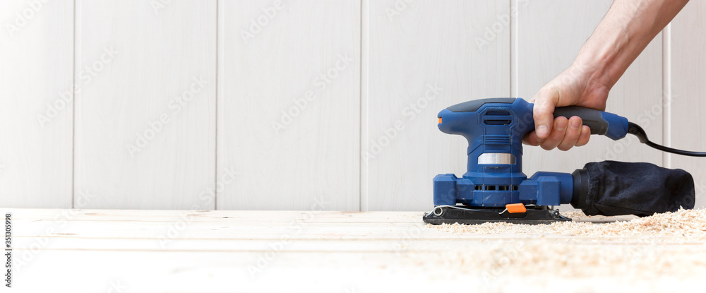 Detail of person working with an electric sander on the natural wooden floor of his house. Space for text. Work, home decoration and DIY concept.