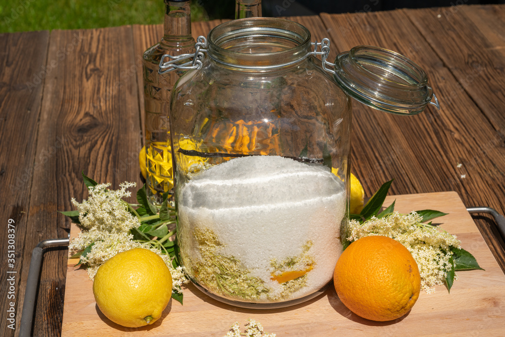 In the large preserving jar on the cutting board are the fresh elderflowers, oranges and lemon slices, sugar and the vanilla pod in the background are the vodka bottles for the elderflower liqueur In the large preserving jar on the cutting board are the fresh elderflowers, oranges and lemon slices, sugar and the vanilla pod in the background are the vodka bottles for the elderflower liqueur