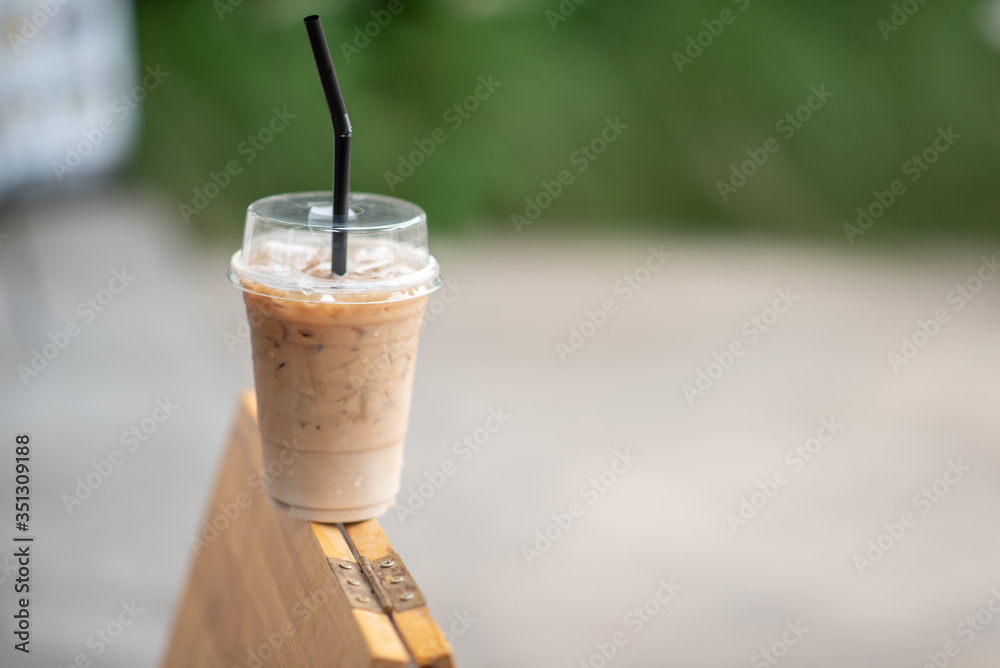 Iced coffee in a clear glass that can see the ice inside the glass and is placed in the coffee shop Green leaf background view Iced coffee in a clear glass that can see the ice inside the glass and is placed in the coffee shop Green leaf background view