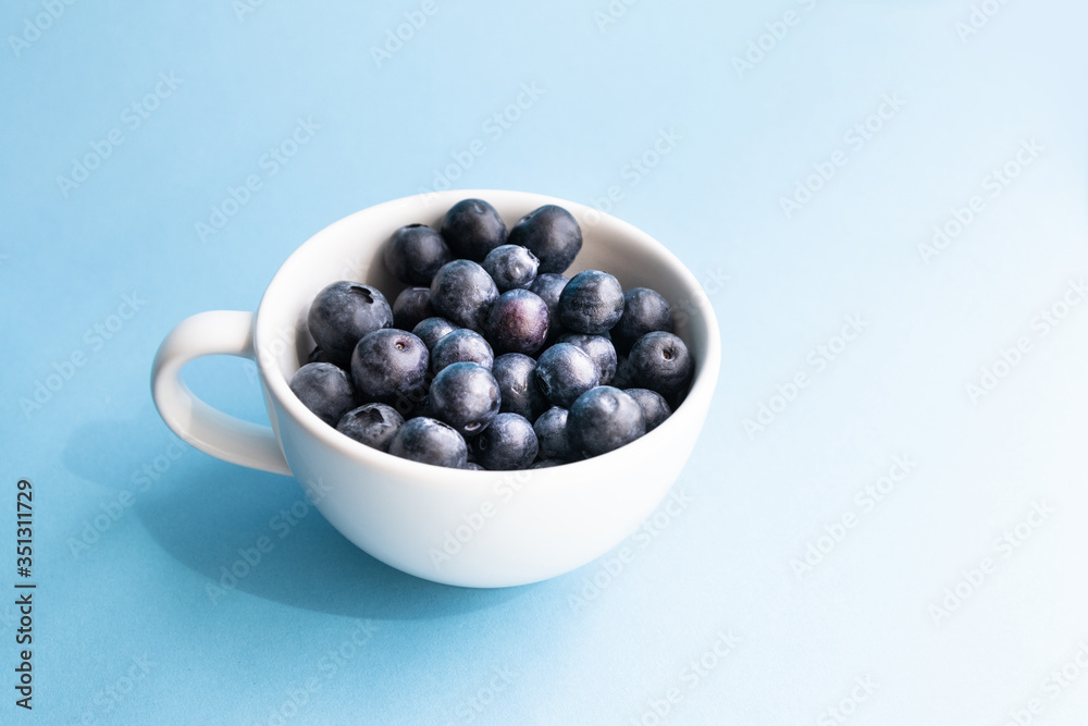 Fresh raw organic blueberry in a mug on blue surface Fresh raw organic blueberry in a mug on blue surface