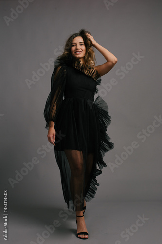 Elegant Young Woman Holding a White Flower in a Black Dress on a Grey Background