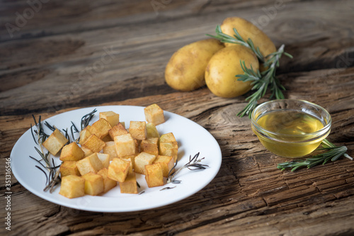 fried potatoes with rosemary and olive oil in a plate on a wooden background and ingredients