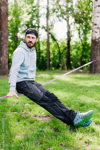 portrait of a young, athletic, bearded guy in a blue hoodie near slackline