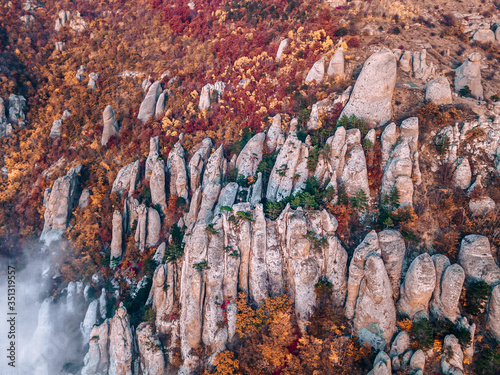 Aerial view of a man standing on the top of sharp rocks amongst autumn forest of the Valley of ghosts on the mountain Demerdzhi, Crimea republic, Russia. photo