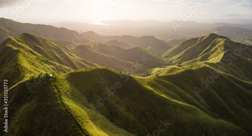 Panoramic aerial view of lush mountain ridge in the golden light of sunrise with the sea in the background. Labawan Peak, Bohol, Philippines
