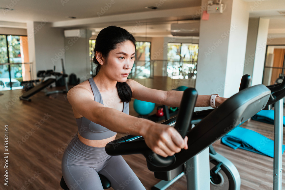 Beautiful young Asian woman doing cardio on a exercise bike at gym