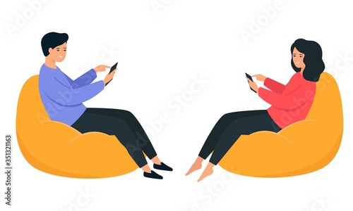 A guy and a girl are sitting on a bean bag chair and holding a smartphone in their hands. Happy young people communicate