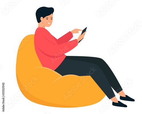 The guy is sitting in a bean bag chair. A young man holds a smartphone in his hand.
