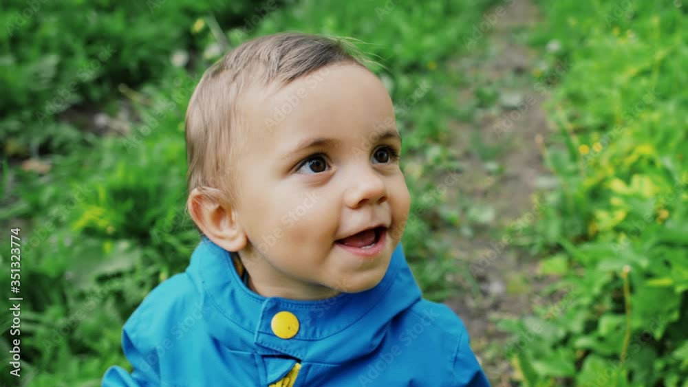 Portrait of adorable baby boy smiling and laughing on green forest background. Cute kid in blue raincoat. Family, love, child concept. Portrait of adorable baby boy smiling and laughing on green forest background. Cute kid in blue raincoat. Family, love, child concept.
