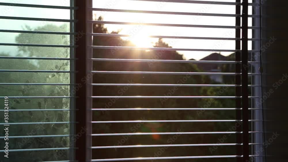 Opening the venetian blinds of the window and seeing sunlight in the morning or evening