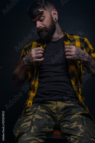 Bearded man with tattoos on his hands and neck wearing yellow black shirt and army pants