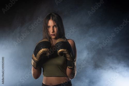 Closeup portrait of a female boxer posing with boxing gloves and looking at the camera with a smokey background