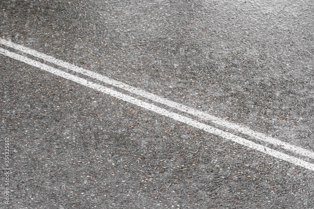 Fototapeta premium Asphalt with two continuous white lines of a road full of water during a rainy day and the drops are splashing the ground