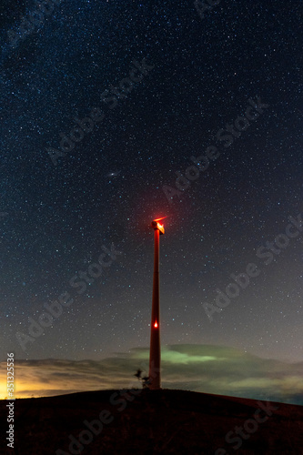 Starry sky with an electric windmill in the middle of a natural landscape
