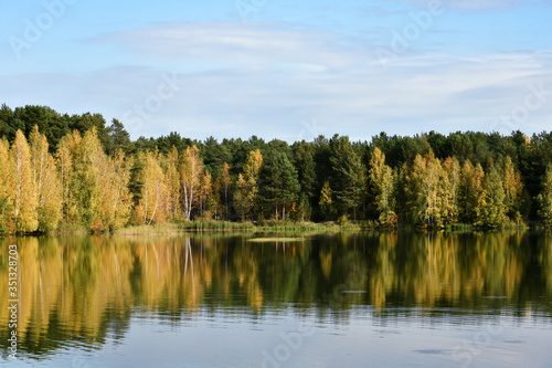 Autumn forest on the lake is full of bright colors against a blue clear sky, reflection in calm water