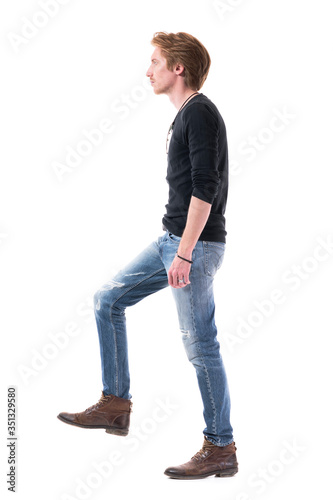 Progress concept. Side view of stylish young man moving up walking upstairs stepping on stairs. Full body length isolated on white background. 