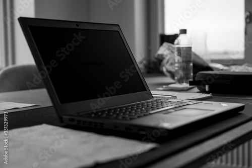A black and white photo of a turned off laptop placed on a kitchen table in a realistic home setting, showing the concept of working from home during quarantine