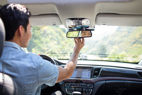 Young man adjusting rear-view mirror in car