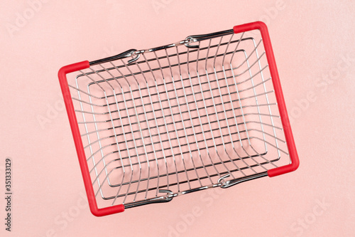 Empty metal shopping basket with red handles, on pink background. Top down view, selective focus on the bottom.