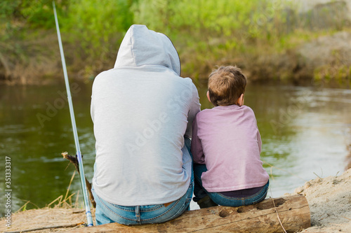 Back view of father and son fishing together, father teaching little young son to be a fisherman near the river. Concept of father's day.