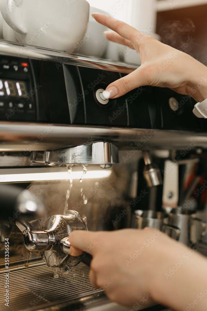 A close photo of a purging a grouphead thoroughly with hot water in the espresso machine in a coffee shop. A female barista works in a cafe.