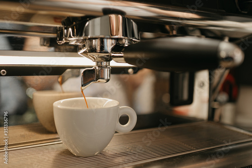 Espresso brewing in a professional espresso machine in a coffee shop. A close-up of a coffee pouring in a white cup from a coffee machine in a cafe.