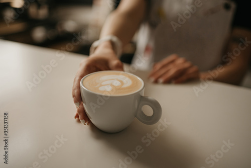 A female barista holds out a cup of hot latte to a client in a cafe. A waitress preparing a customer order. 