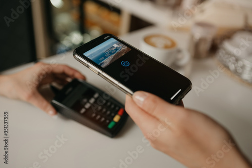 A lady paying for her latte with a smartphone by contactless PAY PASS technology in a cafe. A female barista holds out a terminal for paying to a client in a coffee shop.