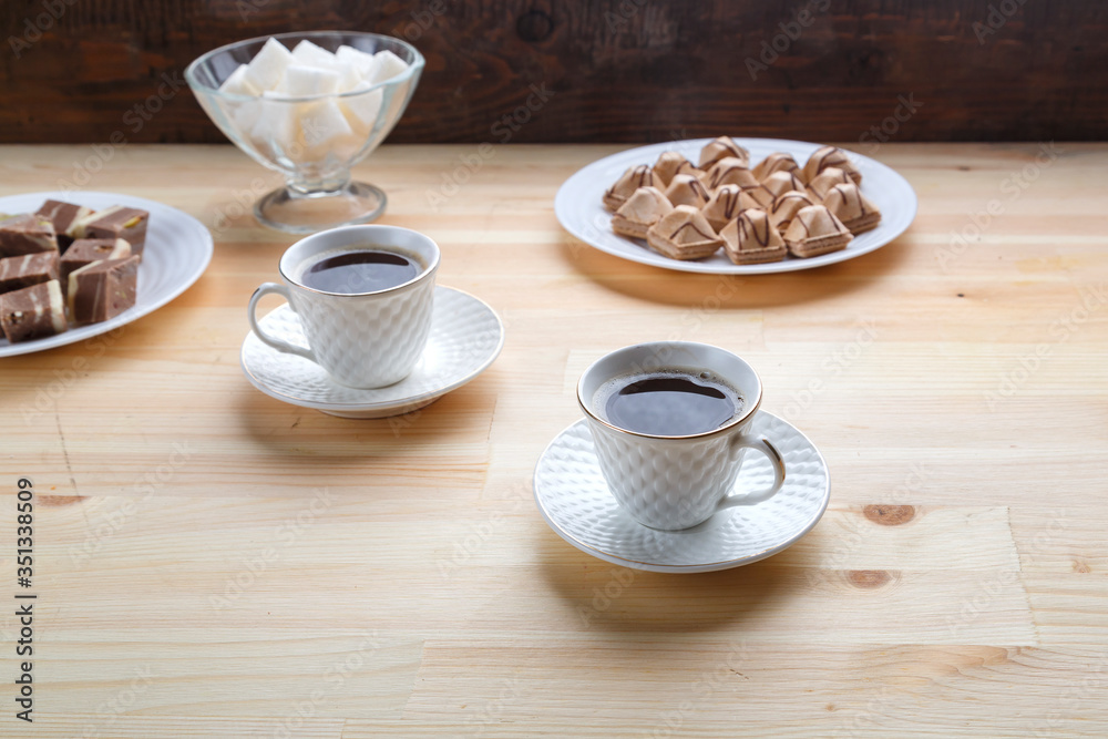 Two cups of coffee on a wooden table with croissants and sugar.