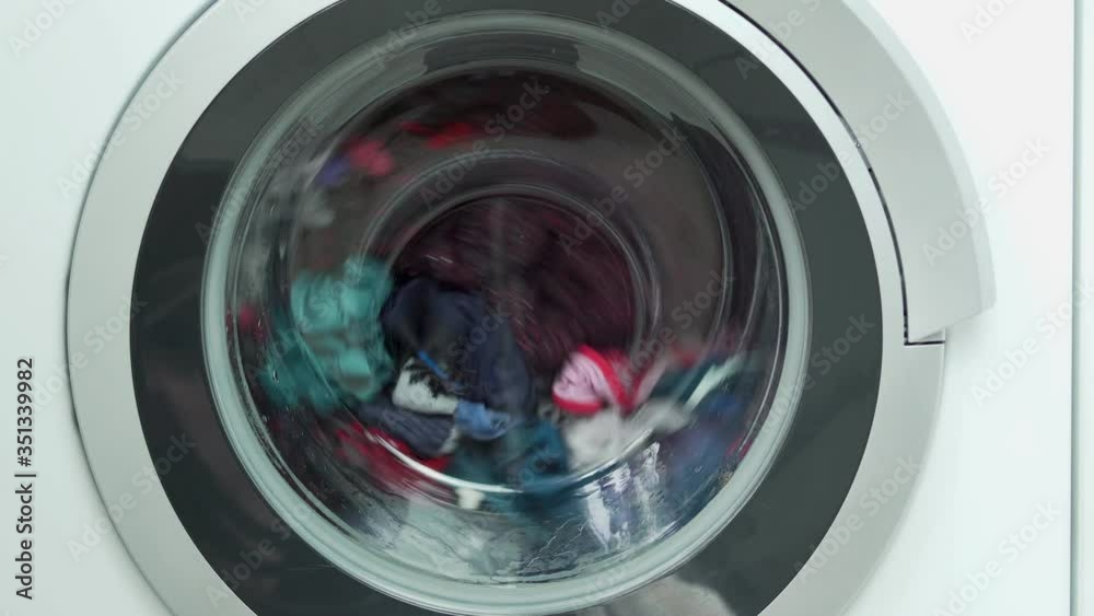 The Process of Rotating the Drum of a Washing Machine with Colored Linen during Washing, Close-up. Washing Machine Operation, Washing Process.