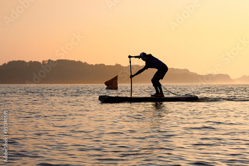 SUP silhouette of teenager standing with a paddle on the surfboard at sunset. Stand up paddle boarding competitions on the calm river © watcherfox