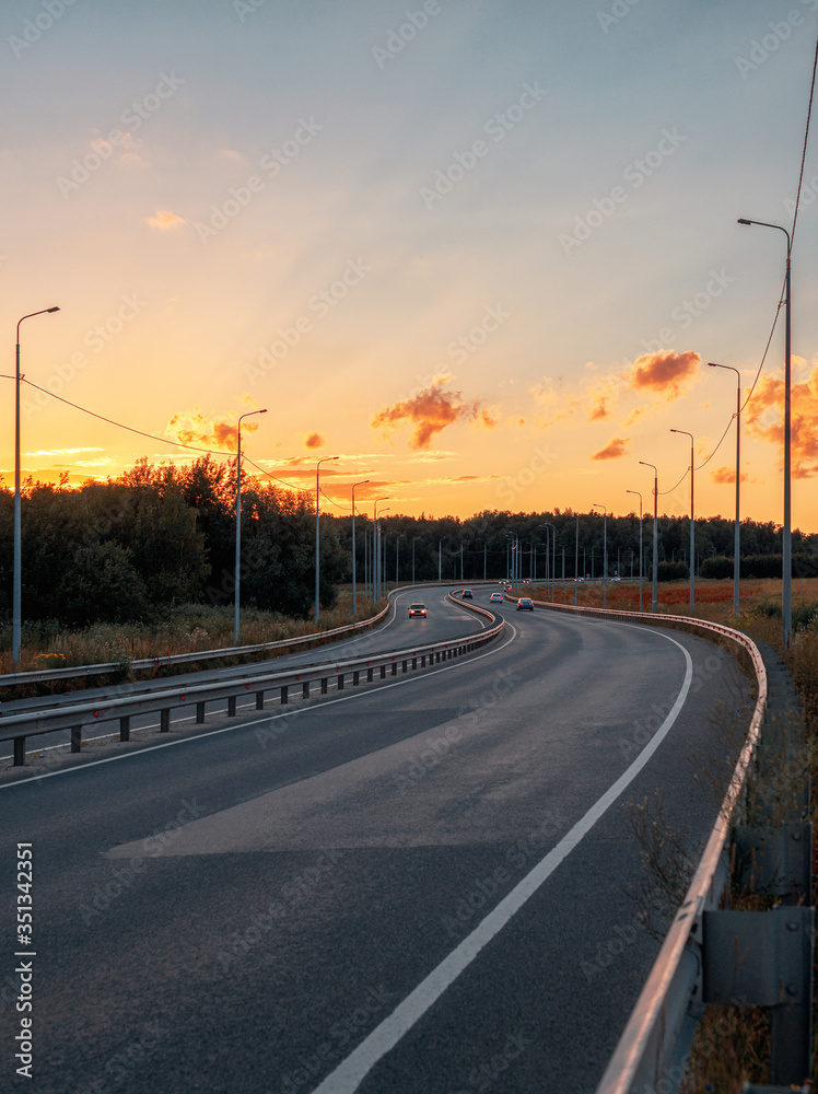The road going into the distance at sunset. Rare cars on the highway. Asphalt road and nature around.