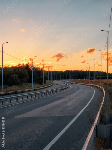 The road going into the distance at sunset. Rare cars on the highway. Asphalt road and nature around.