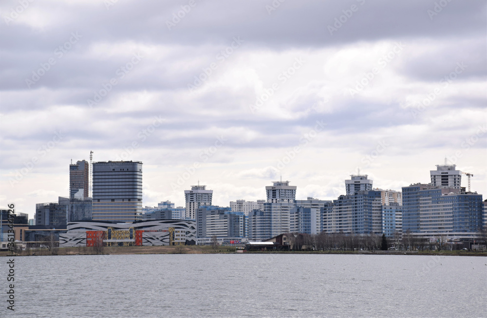 panorama of modern buildings across the river against a dark gray sky, urban architecture, urbanization