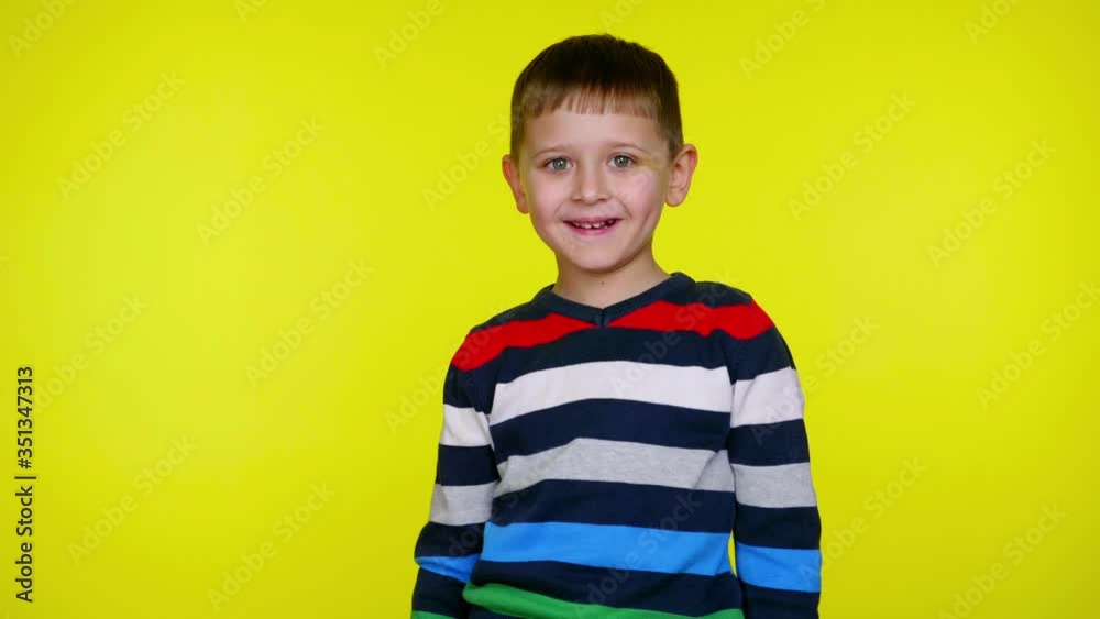 Cheerful little child boy in a multi-colored sweater smiles and looks at the camera on a yellow background with copy space. Place for text or product. 4K slowmotion footage Cheerful little child boy in a multi-colored sweater smiles and looks at the camera on a yellow background with copy space. Place for text or product. 4K slowmotion footage