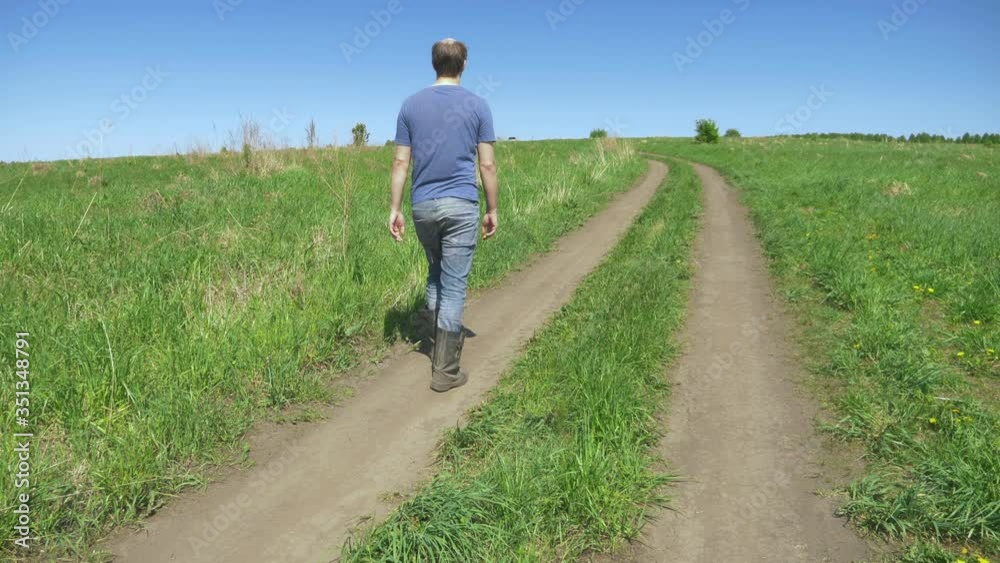 rear view. bald villager in tarpaulin boots walking on a field road rear view. bald villager in tarpaulin boots walking on a field road