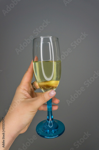 Woman holding Champagne glass with bubbles in hand for visitor. Pouring champagne into color glass at hen-party and making a toast. Wine tasting close up. Celebrate a holiday with low alcohol drink