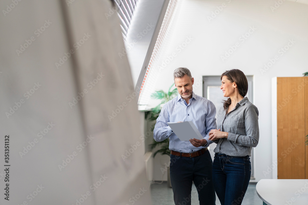 Businessman and businesswoman discussing paper in office Businessman and businesswoman discussing paper in office