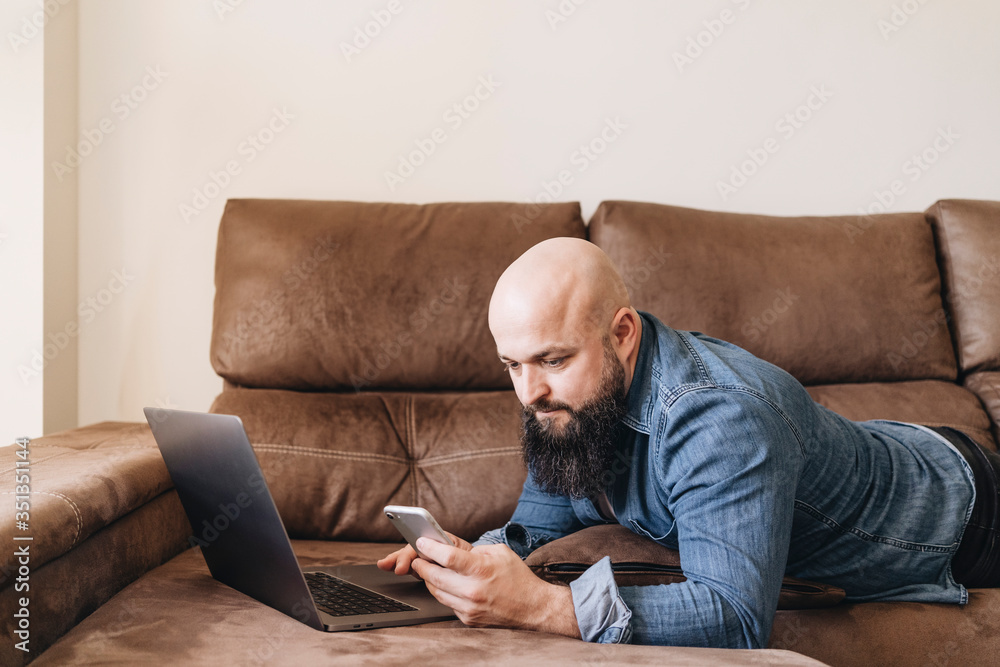Businessman with laptop using mobile phone while lying on sofa at home Businessman with laptop using mobile phone while lying on sofa at home