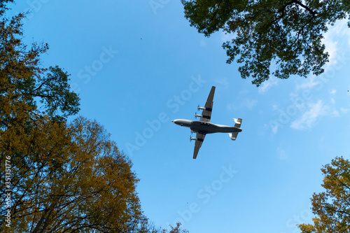 A large plane flies in the blue sky among the tops of autumn trees. Sunny day.