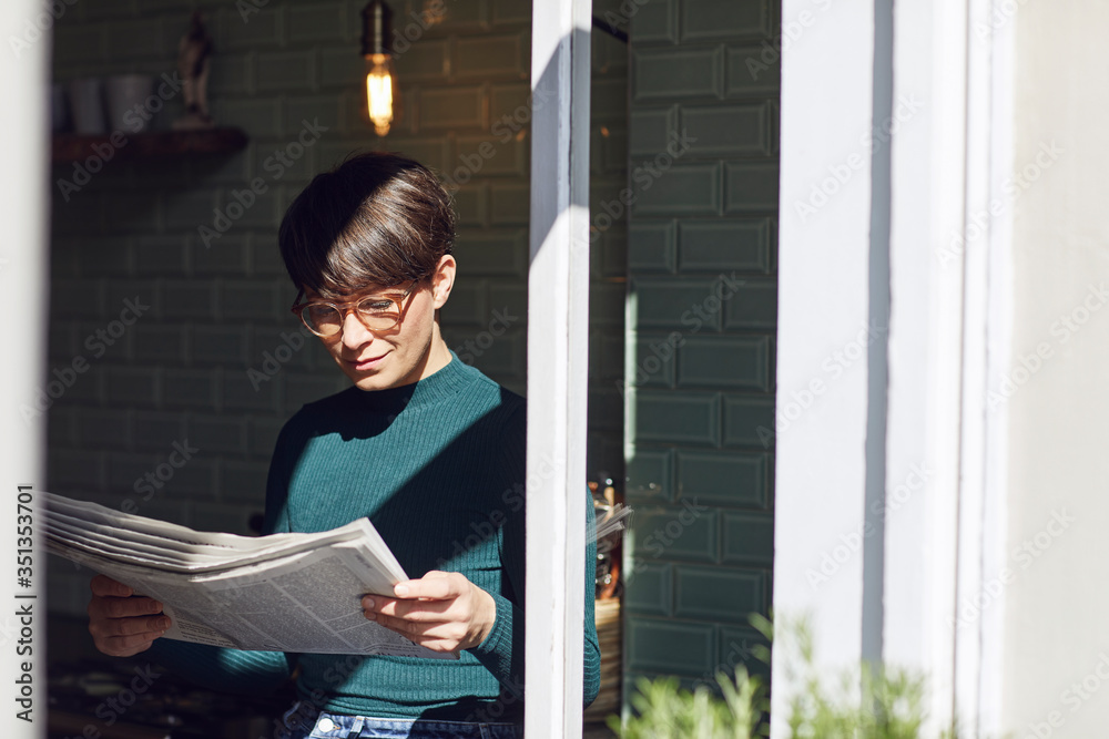 Woman standing at the window at home reading newspaper Woman standing at the window at home reading newspaper