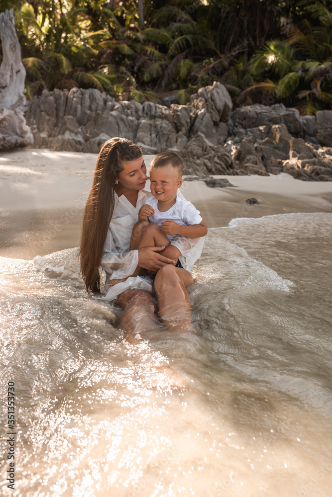 Fototapeta premium Happy smile european family have rest and run on white sand beach. Father, long black chestnut hair mother, blond baby boy. white cotton clothes. boho dress. t-shorts.Thailand. Aquamarine crystal sea