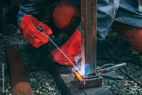 A welder welds a metal pole with electric welding, holds an electrode in his hands
