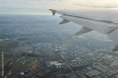 View over the clouds from the porthole of an airplane with plane wing over the Paris Airport area at take off